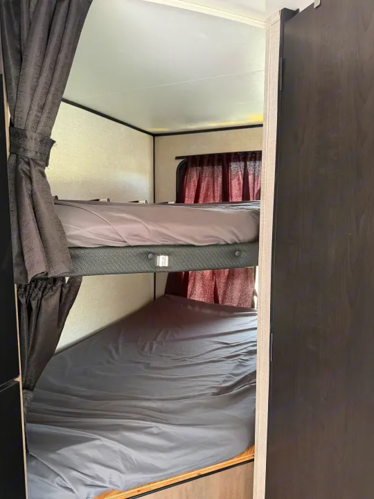 A view inside an RV rental showcasing two neatly made bunk beds with gray bedding and privacy curtains, ideal for family travel.. Autumn Ridge 188BHS 2025