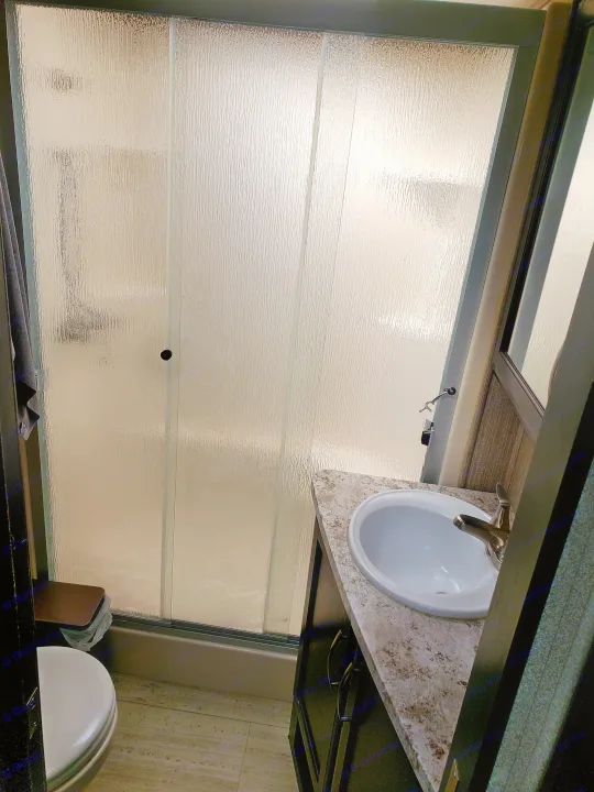 An RV rental bathroom showing a compact shower with textured glass, a sink on a vanity, and a partial view of a toilet.. Grand Design Momentum 2017
