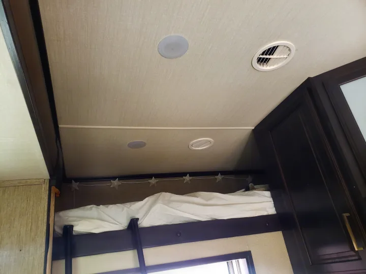 Cozy RV rental interior: upper bunk with white bedding, star lights, ceiling speakers, and air vents.. Grand Design Momentum 2017