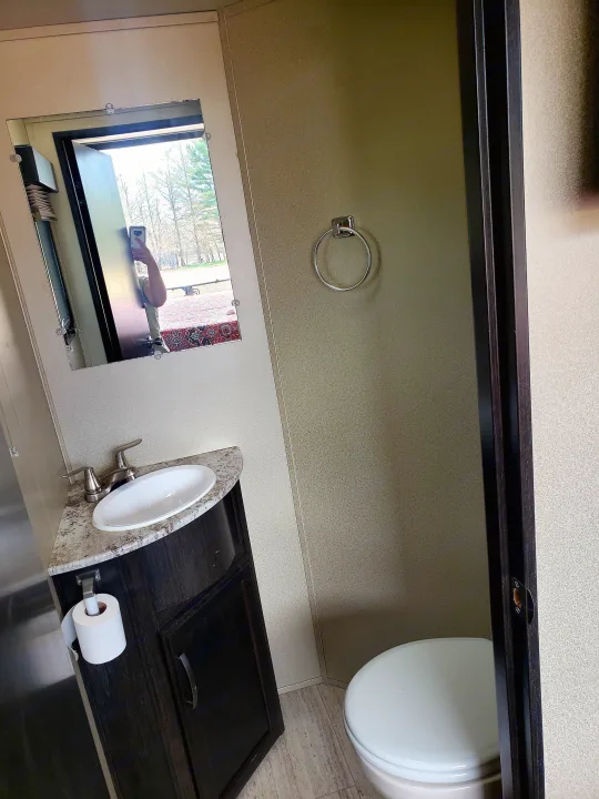 Compact RV rental bathroom features a sink, toilet, and mirror reflecting the scenic outdoor view.. Grand Design Momentum 2017