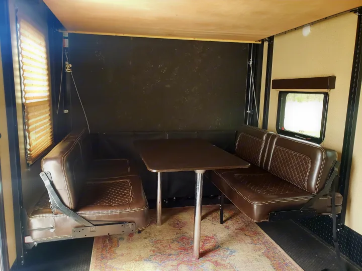 Flexible RV rental interior featuring convertible brown leatherette booth seating and a dining table with a light wood ceiling.. Grand Design Momentum 2017