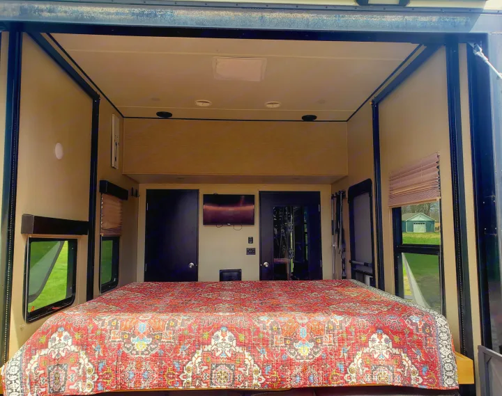 Spacious RV rental bedroom with a large, patterned bed and windows, ideal for comfortable travel.. Grand Design Momentum 2017