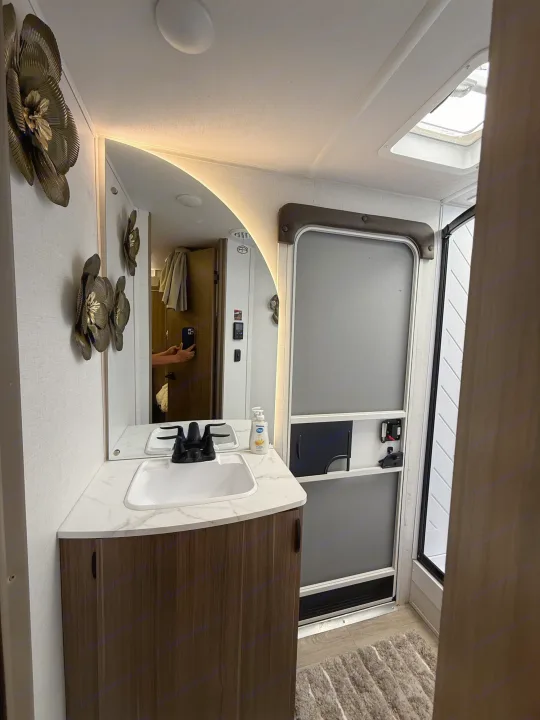 RV rental bathroom view: vanity with white sink, dark faucet, and backlit mirror. An adjacent shower stall and wall decor define the compact space.. Forest River Salem Cruise-Lite 2026