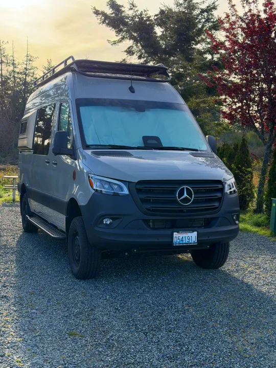 Gray Mercedes-Benz Sprinter camper van, ideal for rv rental, parked on gravel surrounded by trees.. Mercedes-Benz Sprinter 2025