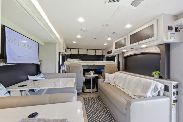 Modern RV rental interior featuring a bright dinette, sofa, overhead bunk, and TV, designed for comfortable travel.. Fleetwood Fortis 2021
