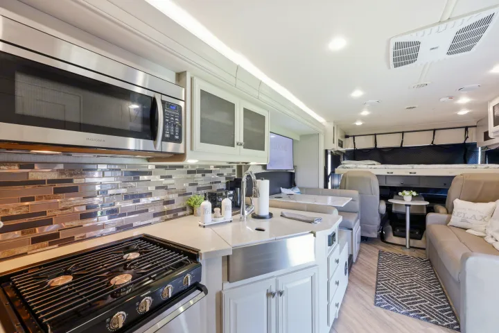 Spacious rv rental interior featuring a modern kitchen with a stove, microwave, and sink, alongside a cozy living area and bunk beds.. Fleetwood Fortis 2021