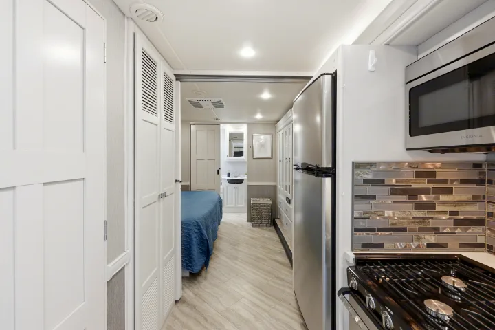 Modern RV rental interior with kitchen (fridge, stove), bedroom with blue quilt, and small bathroom vanity. Ideal for travel.. Fleetwood Fortis 2021