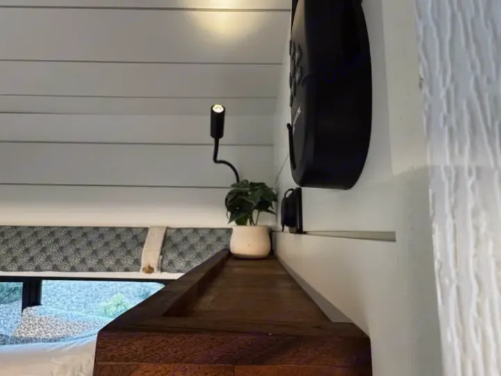 Cozy RV rental interior featuring a bed, small plant, reading light, and control panel on white shiplap walls.. Dodge Other 2023