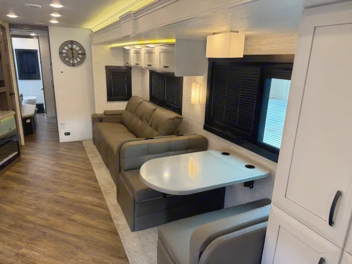 Cozy RV rental interior shows a modern living area with a sofa, dinette, and wood-look flooring. Bathroom visible.. Entegra Coach Accolade 2025