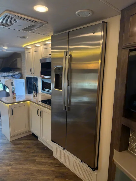 Modern RV rental kitchen featuring a large stainless steel refrigerator, microwave, white cabinets, and a countertop cooktop.. Entegra Coach Accolade 2025