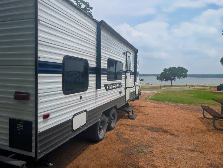 Kingsport travel trailer rv rental parked lakeside on gravel. Experience scenic outdoor camping by the water.. Gulf Stream Kingsport 2022