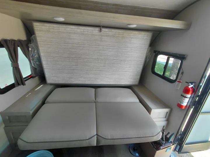 Clean RV rental interior: a versatile bed with built-in storage, side windows, and a safety fire extinguisher. Ready for travel!. Coachmen Catalina Summit Series 2024
