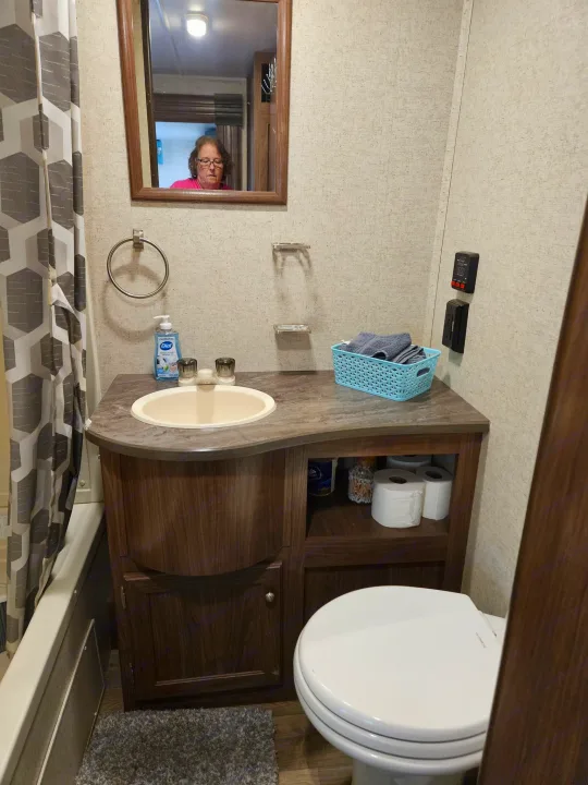 Compact RV rental bathroom with vanity, sink, mirror (reflecting a person), toilet, and shower curtain.. Heartland RVs Prowler 2018