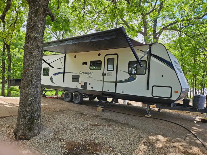 Relaxing at a wooded campsite with our RV rental, a Prowler Lynx travel trailer, under the extended awning.. Heartland RVs Prowler 2018