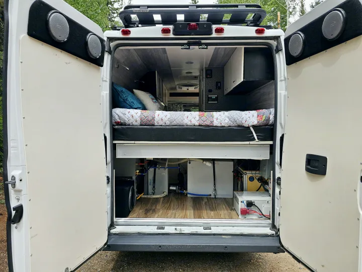 This RV rental showcases a custom campervan interior with a comfy bed, overhead storage, and visible off-grid utility systems.. Dodge Ram ProMaster 3500 2018