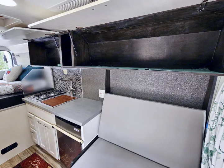 This RV rental's interior features a compact kitchenette with stove, sink, fridge, overhead storage, bed, and seating.. Dodge Ram ProMaster 3500 2018