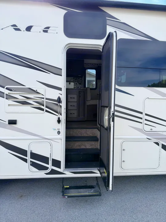 An open door reveals the inviting interior of an RV rental, with entry steps, a kitchen, and a dinette for your travels.. Thor A.C.E. 2018
