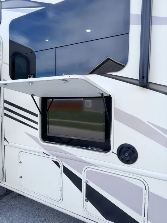 An rv rental's side with an open compartment revealing an outdoor TV & speaker, plus lower storage.. Thor A.C.E. 2018