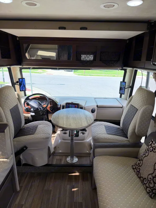 Inside a modern RV rental: the driver's cockpit, a central table, and plush seating in the living area are visible.. Thor A.C.E. 2018