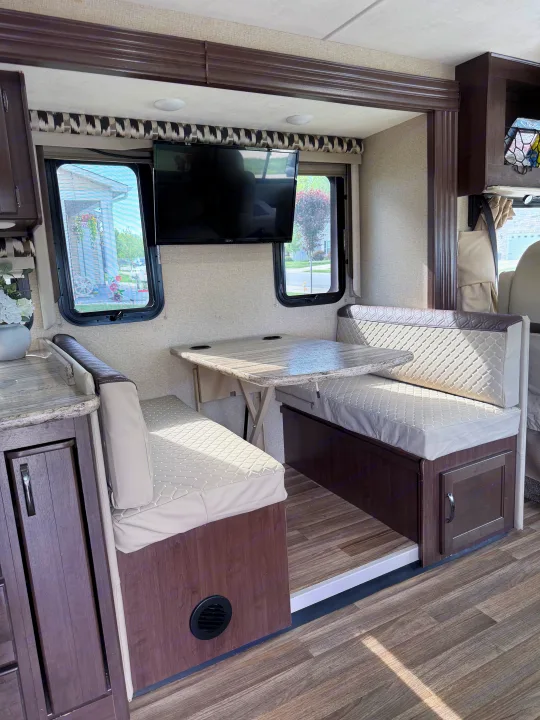 RV rental interior: cozy dinette area with quilted benches, wall-mounted table with cup holders, and TV. Ideal for travel.. Thor A.C.E. 2018