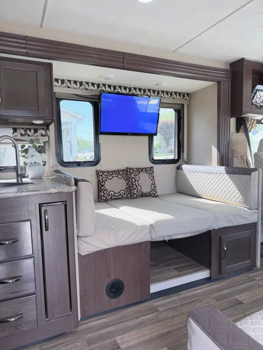 Modern RV rental interior with a dinette that converts to a bed, a TV, and a functional kitchen area.. Thor A.C.E. 2018