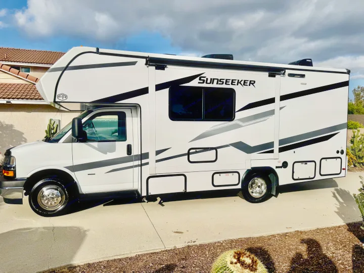 White Sunseeker Class C rv rental with black/gray graphics, parked on a concrete driveway, ready for adventure.. Forest River Sunseeker 2026