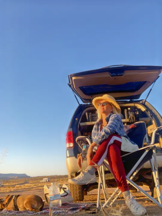 Woman with dog unwinds by SUV, trunk open, during desert camping. A distant RV rental promises more outdoor travel fun.. Ford Campervan Expedition Adventure 4x4 Camper Van Conversion 2007