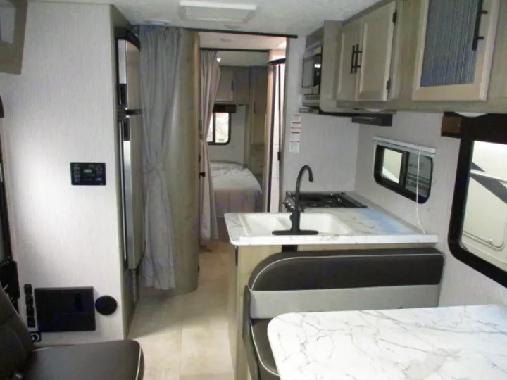 RV rental interior showcasing a kitchen with sink/stove, a dinette, and a bedroom area with a bed and privacy curtain.. Coachmen Freelander 2022
