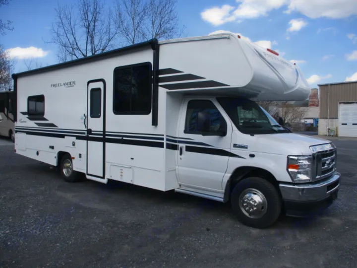 This white Freelander Class C rv rental, featuring black stripes, is parked on a gravel lot, ready for adventure.. Coachmen Freelander 2022