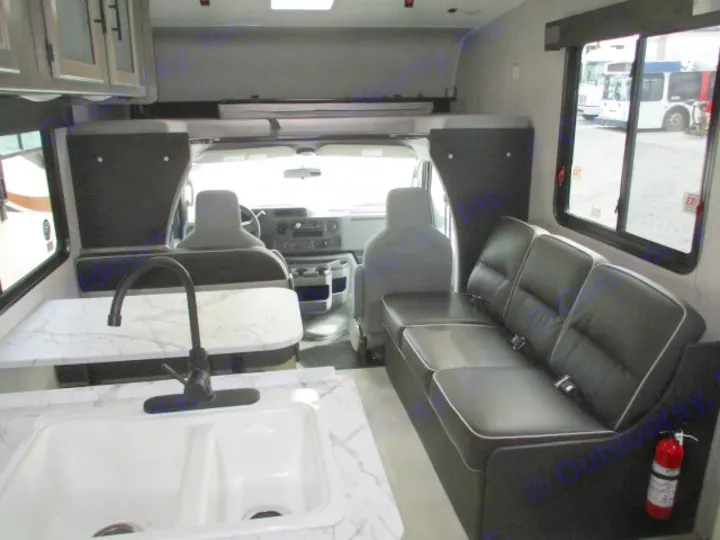 Inside this rv rental, view a kitchen with a double sink, a long black sofa, a dining counter, and the front driver's cab area.. Coachmen Freelander 2022