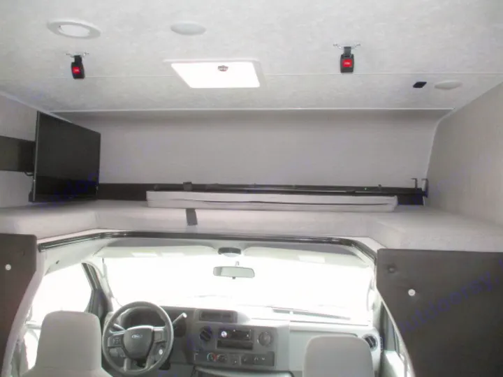RV rental interior: This motorhome shows an over-cab bunk bed with mattresses, a mounted TV, and the vehicle's driver cabin.. Coachmen Freelander 2022