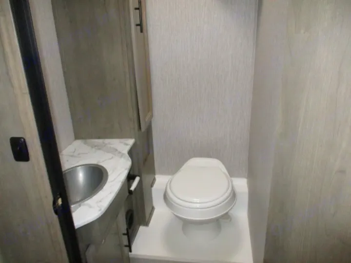 RV rental bathroom with a white toilet, round metal sink, marble-look counter, and wood-textured walls and cabinetry.. Coachmen Freelander 2022