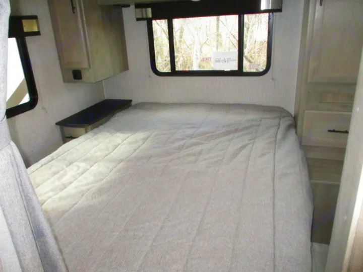 RV rental bedroom interior with a large bed, window overlooking trees, and practical built-in storage solutions.. Coachmen Freelander 2022