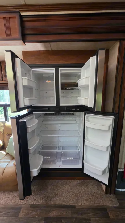 Spacious, empty RV rental refrigerator and freezer combo unit with doors open, showcasing clean shelves and drawers.. Keystone RV Raptor Toy Hauler 2015