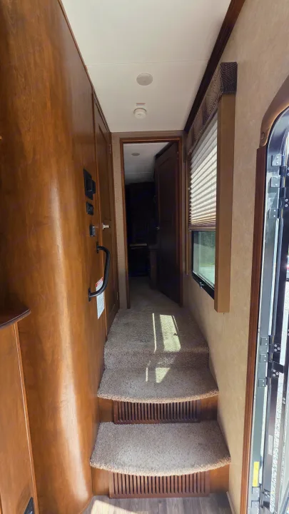 RV rental: Interior hallway with carpeted steps ascending, wooden wall on left, window & entry door on right, doorway ahead.. Keystone RV Raptor Toy Hauler 2015