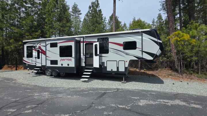 Spacious Raptor fifth-wheel RV rental, parked among pine trees, ready for your next adventure or camping trip.. Keystone RV Raptor Toy Hauler 2015