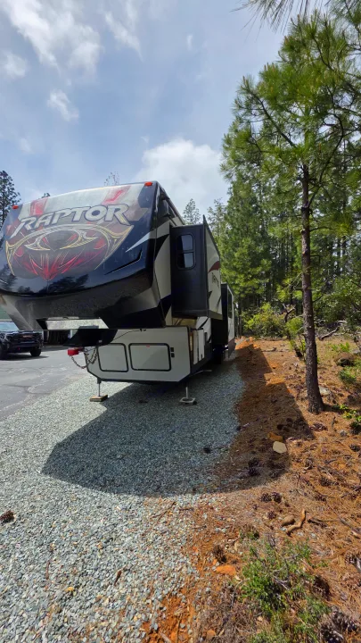 Large black & white Raptor fifth-wheel RV parked on gravel, slides out, next to pine trees. Ideal for an RV rental escape.. Keystone RV Raptor Toy Hauler 2015