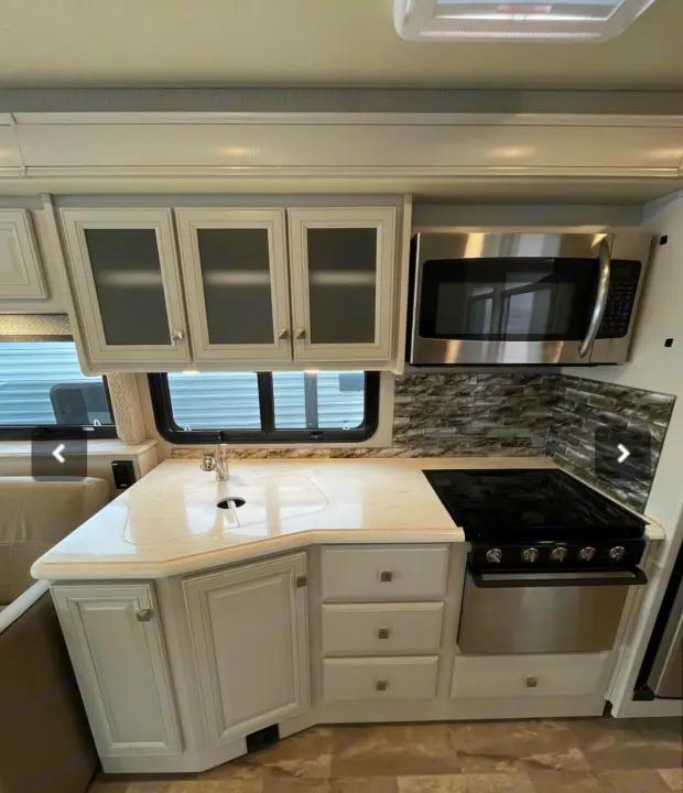 Bright & modern RV rental kitchen: light cabinets, stainless microwave, sink, & electric stove/oven combo.. Holiday Rambler Admiral 2021