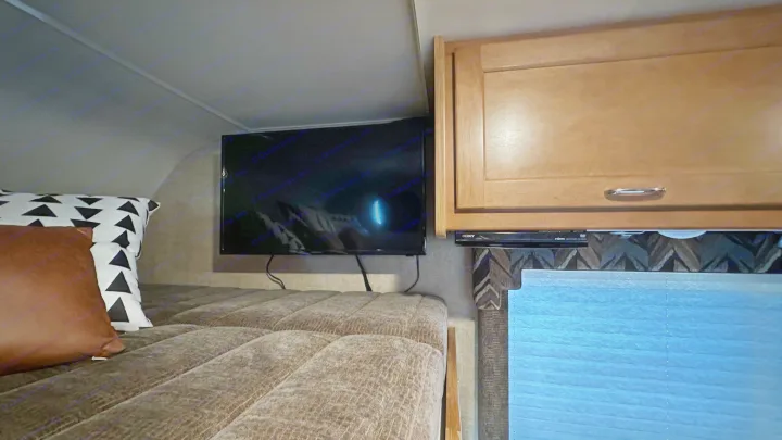 Cozy RV rental interior: A plush bed with decorative pillows, a wall-mounted TV, and wooden cabinets provide comfort and convenience.. Winnebago Minnie Winnie 2018