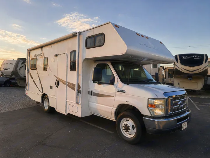 This white Majestic Class C RV rental, a Ford E-350, is parked in a lot with other RVs under a sunset sky.. Thor Majestic 2013