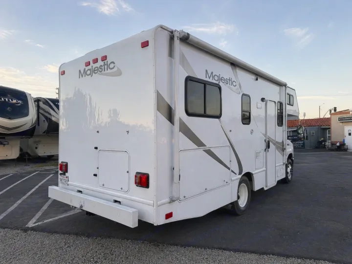 A white Majestic Class C RV rental, featuring grey graphics, parked in a lot. Rear and side view shown under clear sky.. Thor Majestic 2013