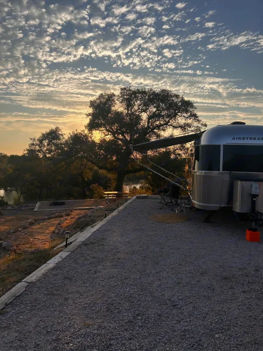 Enjoy this Airstream rv rental campsite at sunset. Features clouds, trees, a fire pit, and water views.. Airstream Flying Cloud 2017