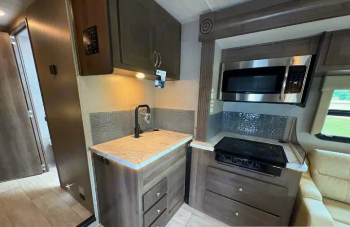 Functional RV rental kitchen with light countertops, black faucet, stainless microwave, stovetop, and storage cabinets.. Nexus RV Phantom 2024
