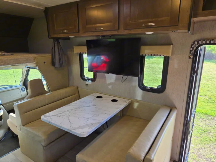 Inside this comfortable **rv rental**: a modern dinette with marble table, TV, overhead cabinets, and a cozy bunk bed up front.. Nexus RV Phantom 2024