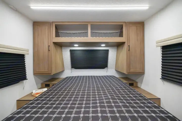Modern RV rental interior: a functional bedroom featuring a plaid bed, overhead storage, and ambient lighting.. Coachmen Freedom Express 19SE 2025