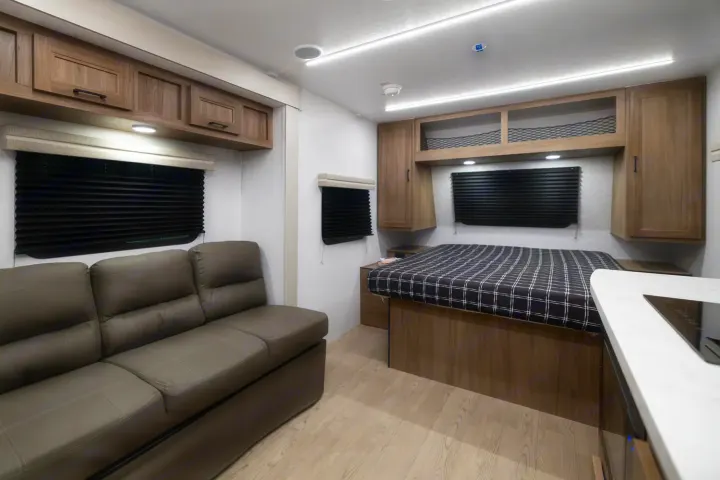 Modern rv rental interior with a gray sofa, a patterned bed, and overhead wood cabinets. Bright and clean.. Coachmen Freedom Express 19SE 2025