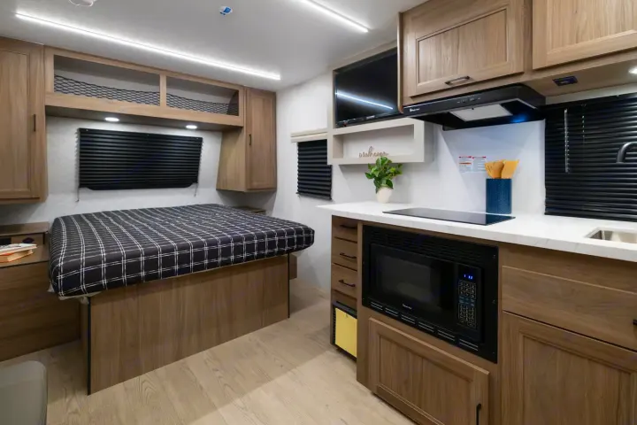 This RV rental interior showcases a cozy bed with overhead storage and a compact kitchen featuring a microwave and stovetop.. Coachmen Freedom Express 19SE 2025