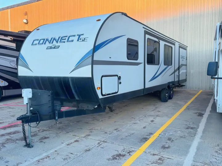 This white KZ Connect SE travel trailer, available for RV rental, features blue graphics and is parked on concrete.. KZ Connect SE 2021