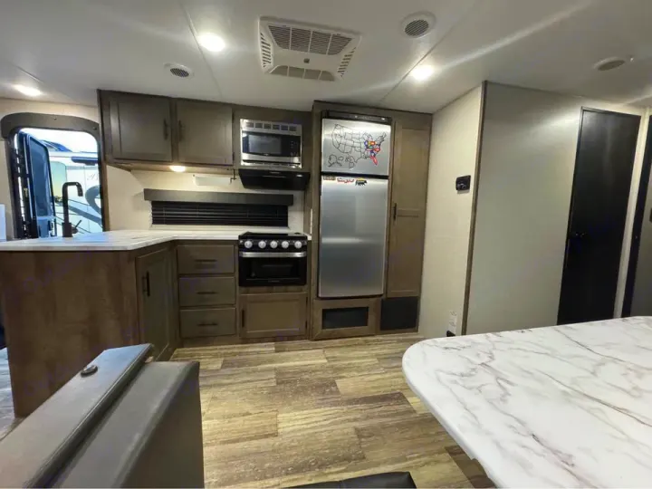 RV rental: Modern kitchen interior featuring wood-tone cabinets, appliances, marble-look counters, and a dining table.. KZ Connect SE 2021