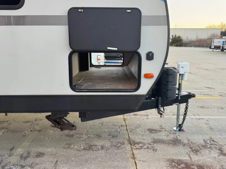 This RV rental travel trailer shows its front section with a large, open pass-through storage compartment. The hitch and a stabilizer jack are visible.. KZ Connect SE 2021